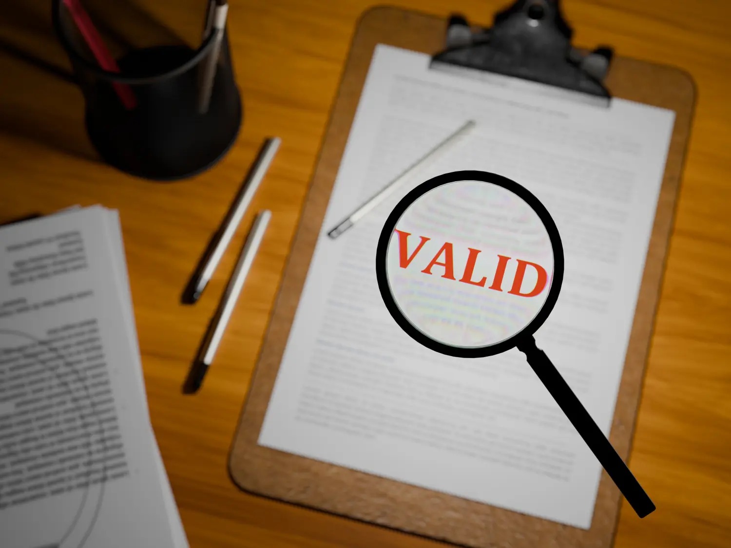 3D-gerenderter Text „VALID“ in fettem Rot unter einer Lupe auf einem Klemmbrett, 3D-gerendert auf einem Tisch.